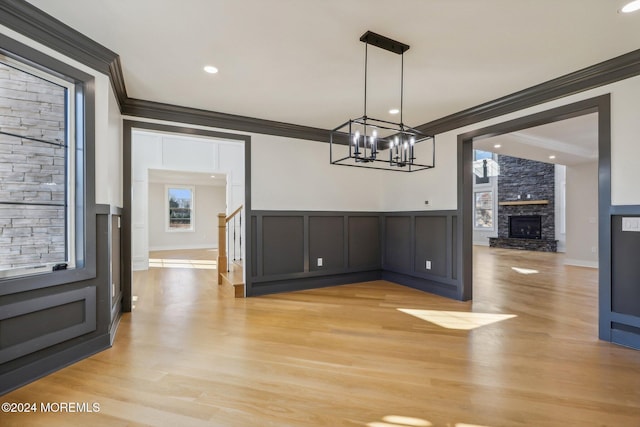 unfurnished dining area featuring light wood-type flooring, a stone fireplace, crown molding, and a notable chandelier