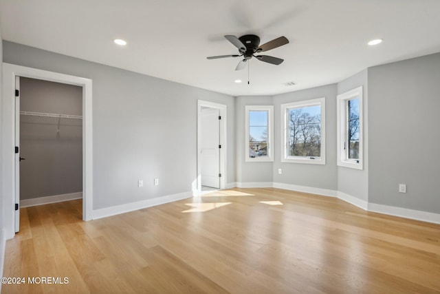 unfurnished bedroom featuring a closet, a walk in closet, ceiling fan, and light hardwood / wood-style flooring