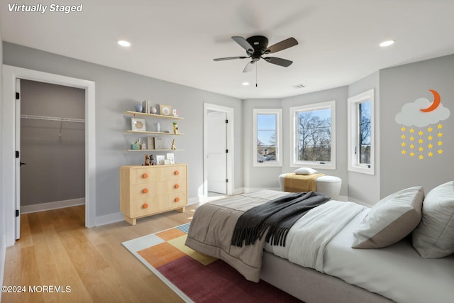 bedroom with a walk in closet, ceiling fan, a closet, and light hardwood / wood-style flooring