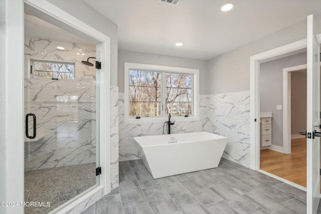 bathroom with plenty of natural light, wood-type flooring, tile walls, and shower with separate bathtub