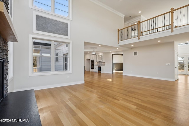 unfurnished living room with a high ceiling, light wood-type flooring, a stone fireplace, and plenty of natural light