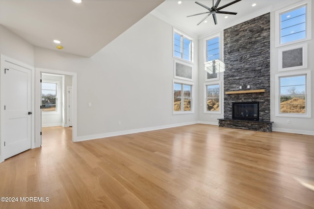 unfurnished living room with ceiling fan, a fireplace, light hardwood / wood-style floors, and a high ceiling