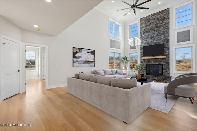 living room with ceiling fan, a stone fireplace, light wood-type flooring, and a high ceiling