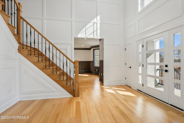 foyer entrance featuring a towering ceiling, ornamental molding, and hardwood / wood-style flooring