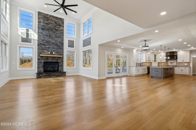 unfurnished living room with light wood-type flooring, ornamental molding, ceiling fan with notable chandelier, a high ceiling, and a stone fireplace