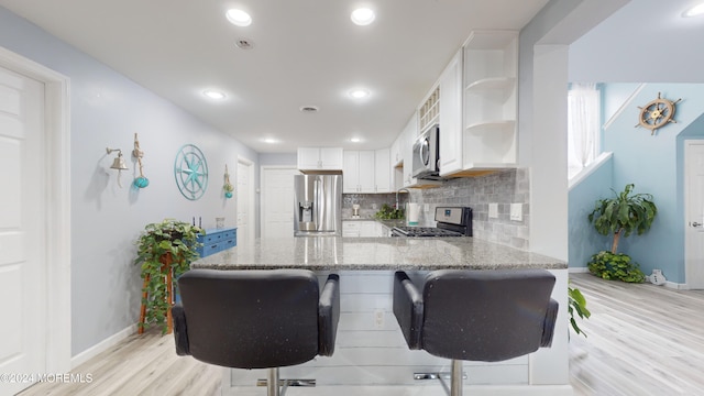 kitchen with a breakfast bar, white cabinets, light stone countertops, kitchen peninsula, and stainless steel appliances