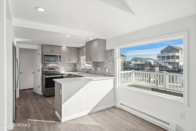 kitchen with baseboard heating, appliances with stainless steel finishes, kitchen peninsula, decorative backsplash, and hardwood / wood-style flooring