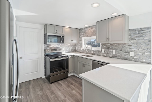 kitchen with kitchen peninsula, light hardwood / wood-style floors, gray cabinets, appliances with stainless steel finishes, and sink