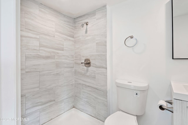 bathroom with toilet, tiled shower, and vanity