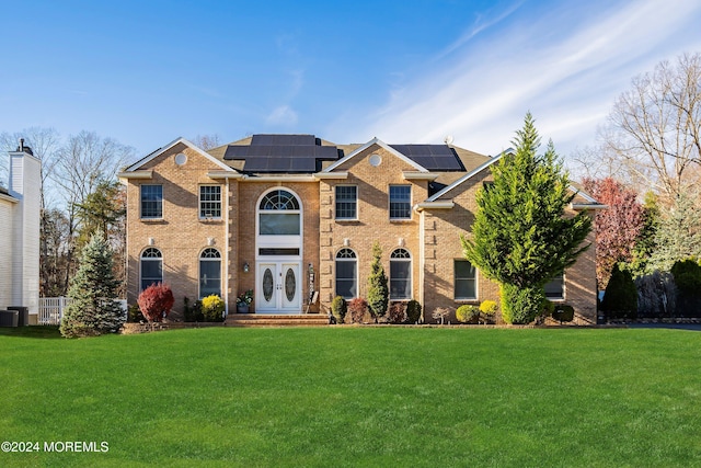 view of front of house with central AC, french doors, a front yard, and solar panels