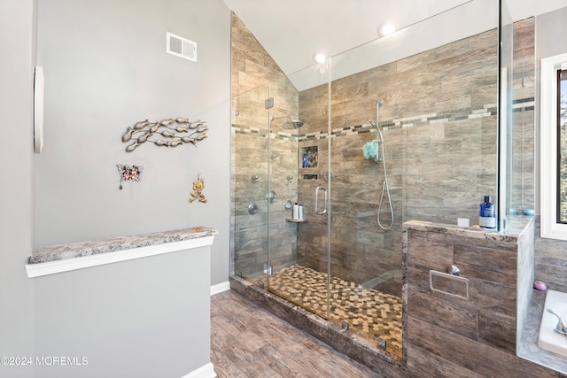 bathroom with wood-type flooring, a shower with door, and vaulted ceiling