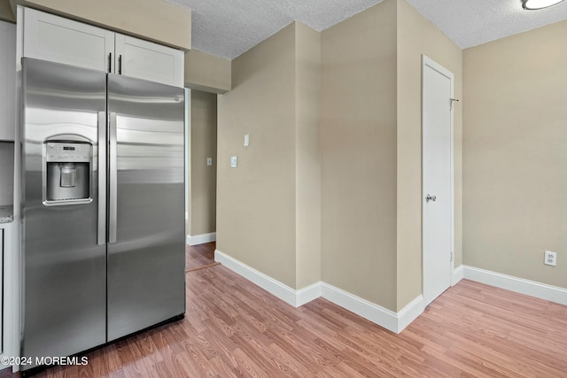 kitchen with stainless steel refrigerator with ice dispenser, a textured ceiling, light hardwood / wood-style floors, and white cabinetry