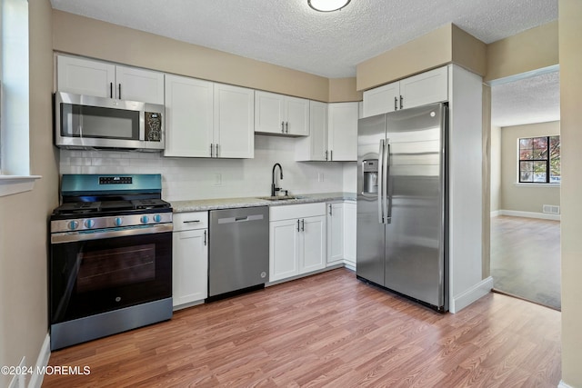 kitchen with white cabinetry, sink, light hardwood / wood-style flooring, decorative backsplash, and appliances with stainless steel finishes