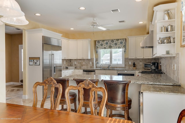 kitchen featuring white cabinetry, light stone countertops, wall chimney exhaust hood, and stainless steel appliances