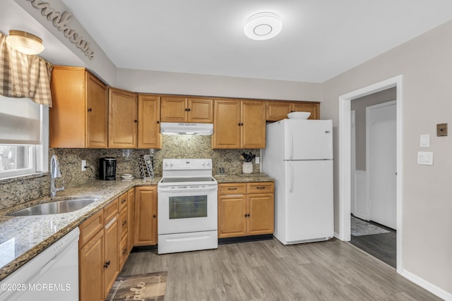 kitchen with white appliances, tasteful backsplash, light wood finished floors, under cabinet range hood, and a sink