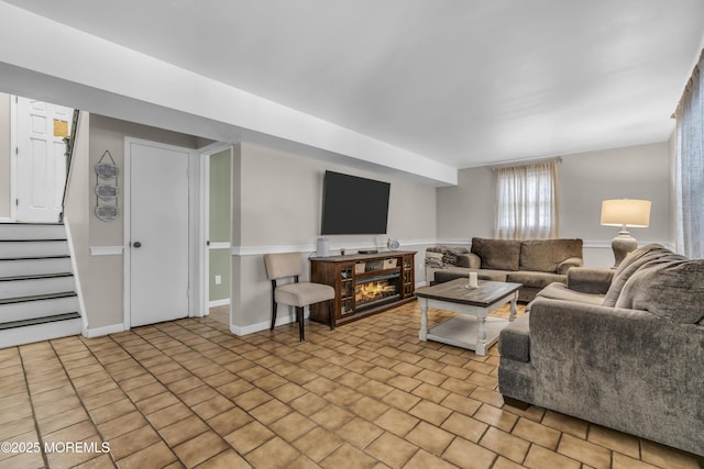 living room featuring a lit fireplace, stairway, and baseboards