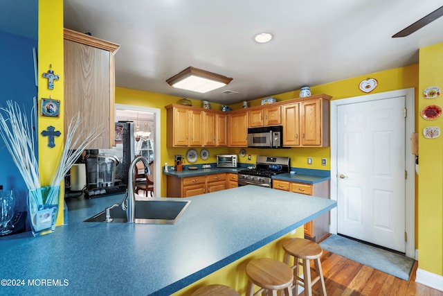 kitchen featuring kitchen peninsula, a kitchen breakfast bar, stainless steel appliances, sink, and hardwood / wood-style flooring