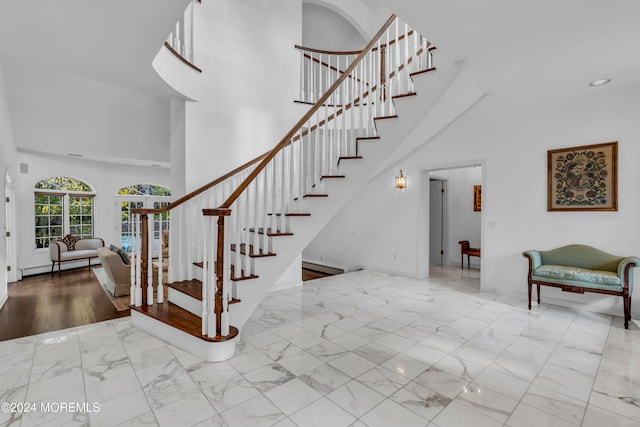 stairway with hardwood / wood-style floors, a towering ceiling, and a baseboard radiator