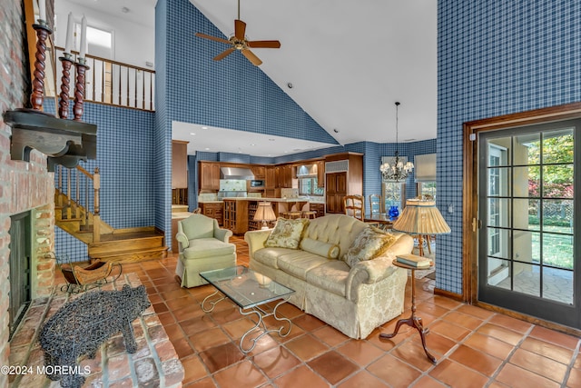 living room with tile patterned flooring, high vaulted ceiling, ceiling fan with notable chandelier, and a brick fireplace