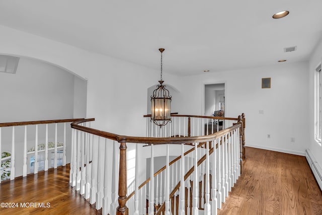 hallway with hardwood / wood-style flooring, a baseboard heating unit, and an inviting chandelier