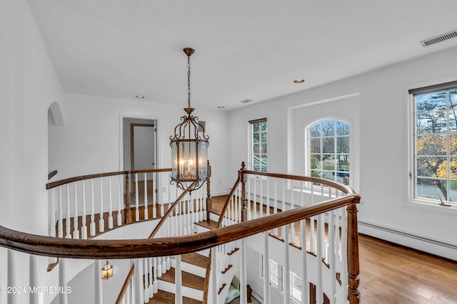 stairway with wood-type flooring, a healthy amount of sunlight, and a notable chandelier