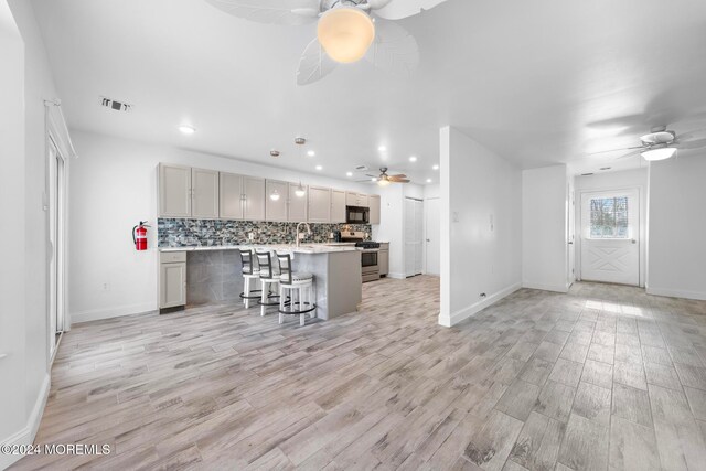 kitchen with a kitchen bar, stainless steel range, a kitchen island, and light wood-type flooring