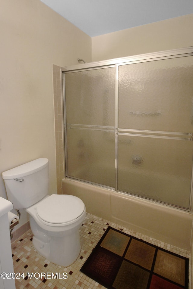 bathroom featuring tile patterned flooring, toilet, and bath / shower combo with glass door