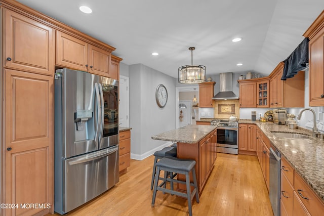 kitchen with appliances with stainless steel finishes, wall chimney exhaust hood, sink, light hardwood / wood-style flooring, and a center island