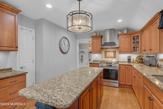 kitchen with gas stove, a center island, wall chimney range hood, an inviting chandelier, and light hardwood / wood-style flooring