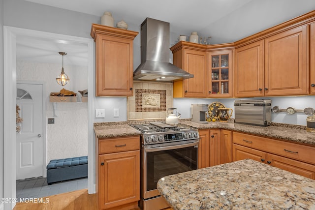 kitchen featuring light stone countertops, stainless steel stove, and wall chimney range hood