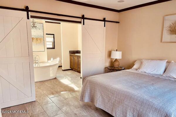 bedroom with a barn door, ensuite bath, and crown molding