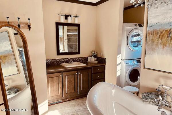 bathroom with a washtub, vanity, crown molding, and stacked washer and clothes dryer