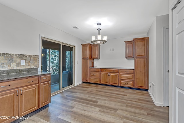 kitchen featuring a notable chandelier, backsplash, dark stone countertops, pendant lighting, and light hardwood / wood-style floors