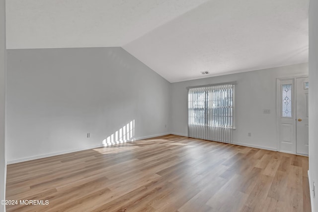 interior space featuring a textured ceiling, light wood-type flooring, and vaulted ceiling