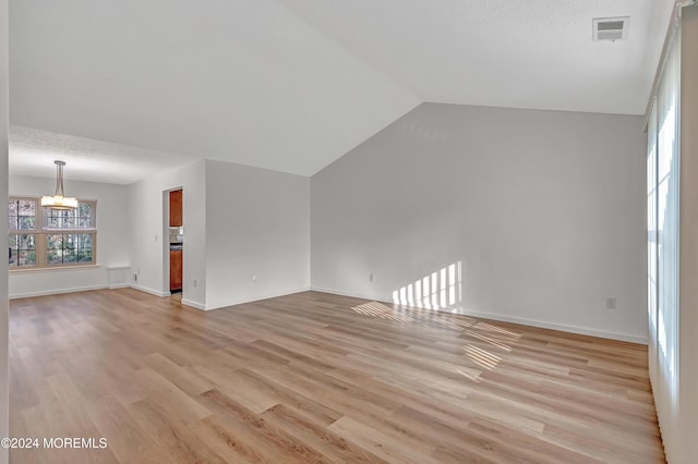 unfurnished living room with a textured ceiling, a chandelier, light hardwood / wood-style floors, and vaulted ceiling