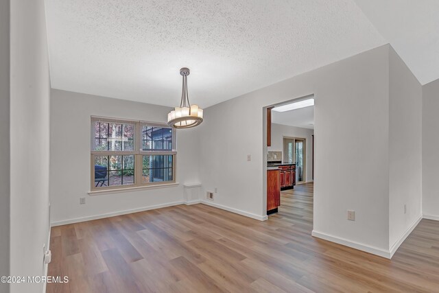 unfurnished dining area with light hardwood / wood-style floors, a textured ceiling, and a notable chandelier