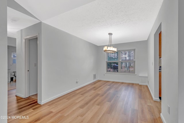 unfurnished dining area featuring light wood-type flooring, a textured ceiling, and an inviting chandelier