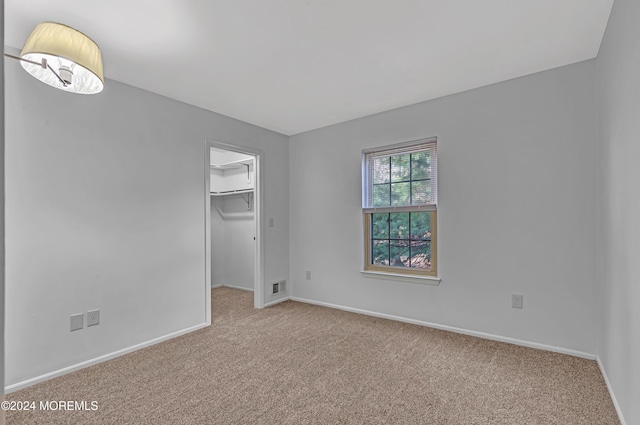 unfurnished bedroom with a walk in closet, a closet, and light colored carpet