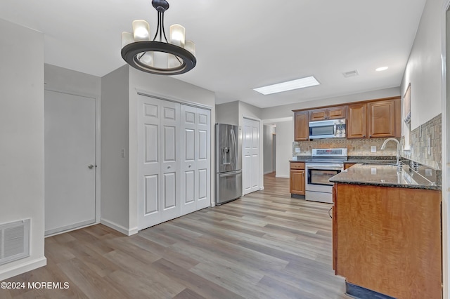 kitchen with pendant lighting, sink, stainless steel appliances, and light hardwood / wood-style flooring