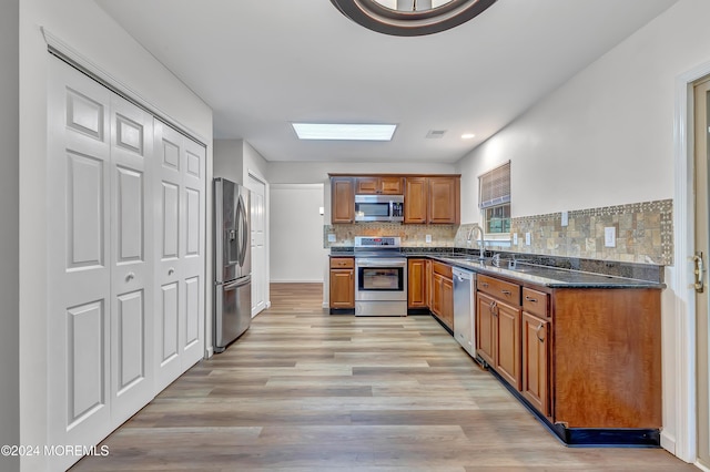 kitchen with backsplash, sink, light hardwood / wood-style flooring, a skylight, and appliances with stainless steel finishes