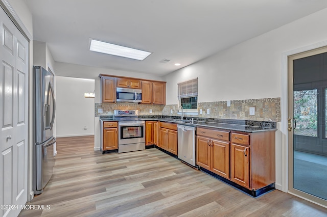 kitchen with decorative backsplash, a skylight, stainless steel appliances, sink, and light hardwood / wood-style flooring