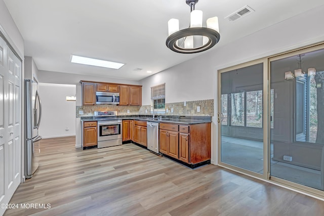 kitchen featuring decorative backsplash, light wood-type flooring, stainless steel appliances, an inviting chandelier, and hanging light fixtures