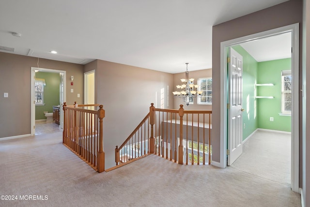 hall with a wealth of natural light, light colored carpet, and an inviting chandelier