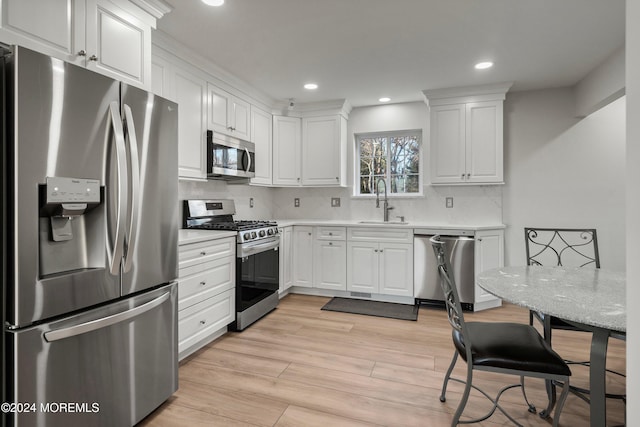 kitchen featuring sink, tasteful backsplash, light hardwood / wood-style floors, white cabinetry, and stainless steel appliances