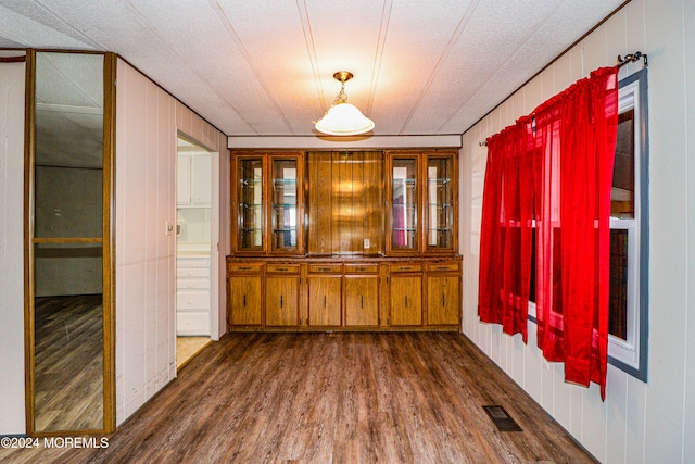 unfurnished dining area featuring a textured ceiling, dark hardwood / wood-style flooring, and wooden walls