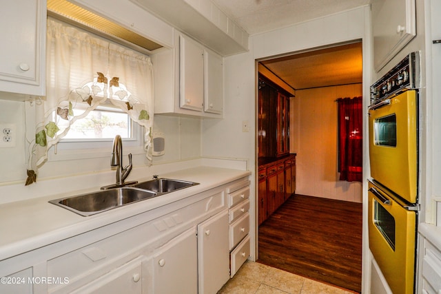 kitchen featuring sink, white cabinets, stainless steel double oven, and light hardwood / wood-style flooring