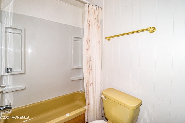 bathroom with shower / bath combo, wood walls, and toilet