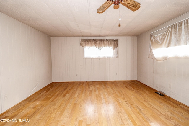 spare room with ceiling fan, wood walls, and wood-type flooring