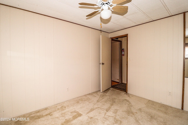 carpeted spare room featuring ceiling fan and wooden walls