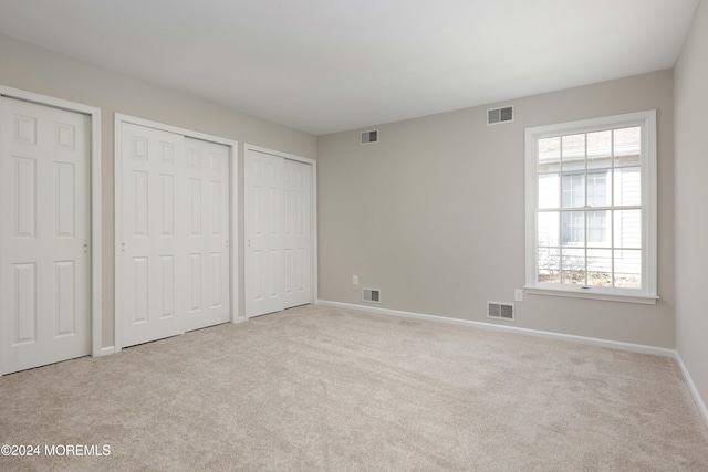 unfurnished bedroom with light colored carpet and multiple closets